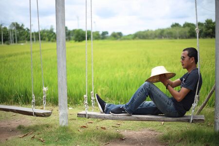 Man sitting on a swing in a rice field Rayong, Thailandの写真素材