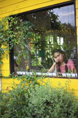 Woman sitting and looking at the garden view through the glass roomの写真素材