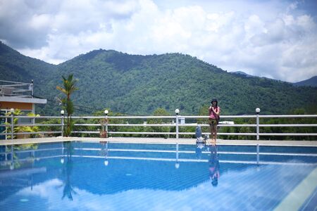 Woman standing at the pool area with mountain viewsの写真素材
