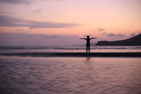 Silhouette of a man standing on the beach at sunset.の写真素材