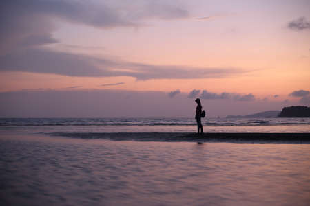 Silhouette of a woman walking on the beach at sunset.の写真素材