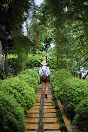A woman wearing a straw hat is walking up the stairs in the garden.の写真素材
