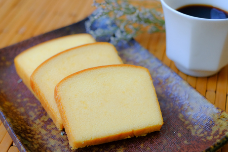 Homemade plain butter cake soft and moist. Slice of butter cake on plate and serve with black coffee on wood tableの写真素材