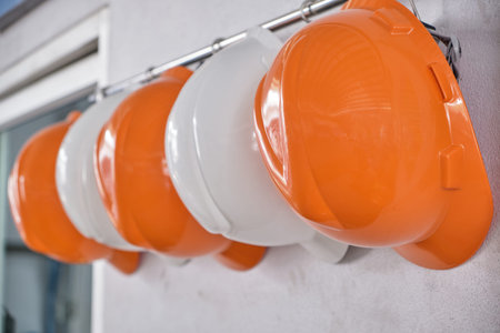 Hard hats hanging on hook against the dirty white wall.