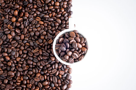 Dark roast coffee beans and the white cup background, top view