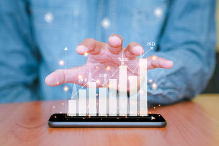 Businessman used a smartphone and touch the screen with business graph pop up on smart phone. The concept of finance and technology.の写真素材