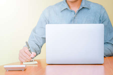 A businessman using a laptop computer to search for information and take notes on paper.の写真素材