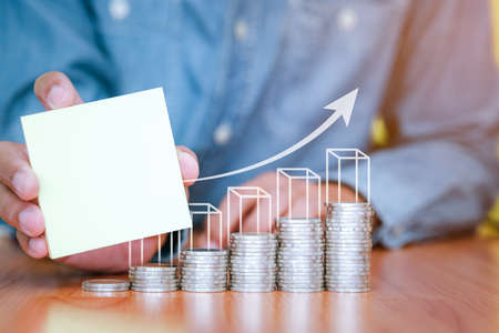 A businessman holding a blank note with coins stack placed on the front. Saving and investment concept for the future. copy space for text.の写真素材