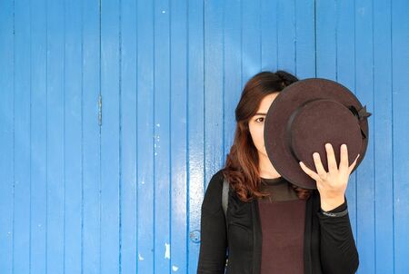 A secret girl who closed half face with a black hat with blue door backgroundの写真素材