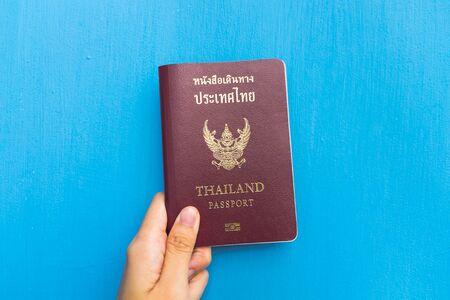 Left hand holding Thailand passport for travel with blue backgroundの写真素材