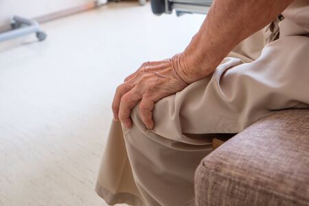 Old senior hands holding on to her knee and sitting in the hospitalの写真素材