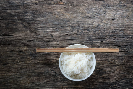 Jasmine rice in the bowl and bamboo chopsticks on wooden.