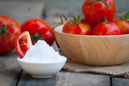 Tometoes group in bowl on wooden table with salt. some person eat fresh tometo for healthy skin, pink, red ginseng.の写真素材
