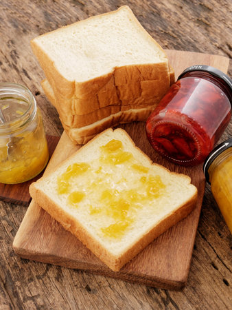 Red strawberry and peach yellow jam on plank wood and slice bread.