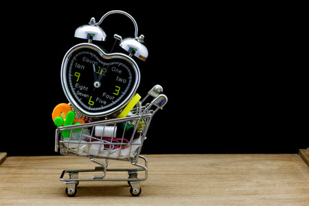 alarm clock with school supplies on shopping cart , black background