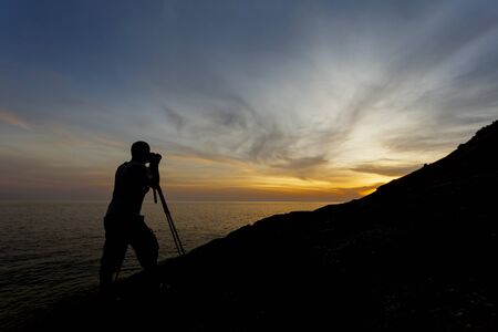 Silhouette of a photographer or traveler using a professional DSLR camera,photographer take sunset photo.の写真素材