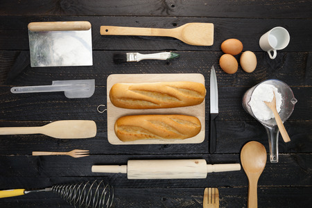 Baking background with bread, flour, rolling pin,eggs,wooden spoons on black wooden background,cooking concept top viewの写真素材