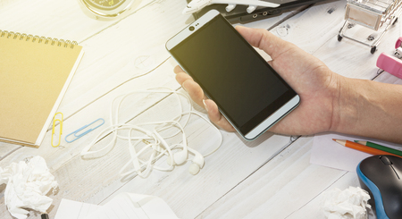 hand male holding smartphone on white wooden office table with business objectsの写真素材
