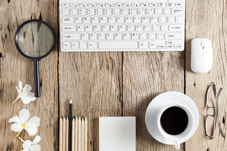 business objects of keyboard,mouse,white coffee cup,white paper,pencils,glasses,magnifying glass and frangipani flowers on old wooden table backgroundの写真素材