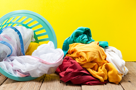 Pile of dirty laundry in washing basket on wooden,yellow backgroundの写真素材