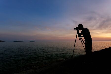 Silhouette of a photographer or traveler using a professional DSLR camera,photographer take sunset photo.の写真素材
