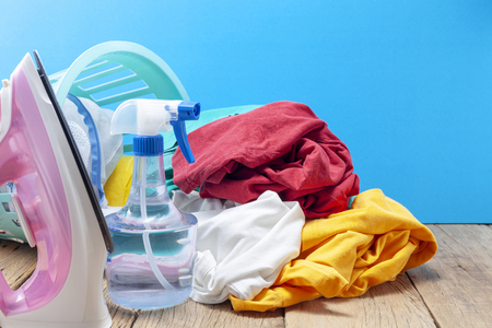 Pile of colorful clothes and irons,spray bottle on wooden plank ,blue color background.の写真素材