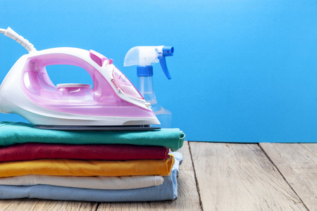 Pile of colorful clothes and irons,spray bottles,on wooden plank ,blue color background.の写真素材