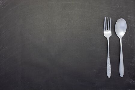 Stainless steel spoon and fork on black wood or chalkboard background.の写真素材