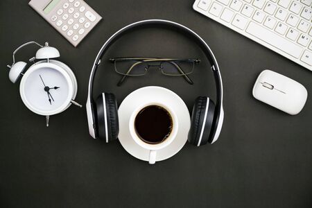 Office desk business objects of white coffee cup,keyboard,headphone,white alarm clock,calculator,mouse and glasses on blackboard.の写真素材