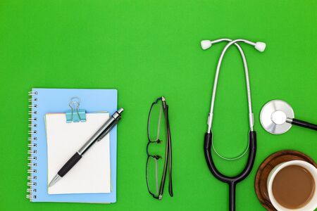 Stethoscope with notebook ,pen, white paper ,coffee cup,glasses, on green background,Medical background conceptの写真素材