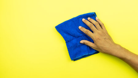 Man hand holding blue microfiber cleaning cloth isolated on yellow background