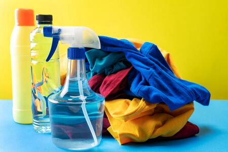 Plastic bottles of cleaning products set with pile clothes on blue table Yellow backgroundの写真素材