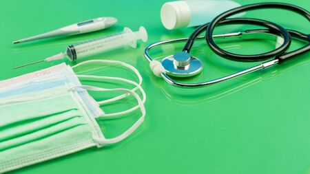 Coronavirus or Covid-19 Medical mask with Stethoscope,Electronic thermometer and syringe on green tableの写真素材