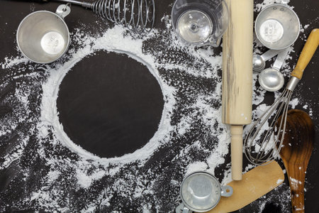 Sprinkle wheat flour with copy space for text on dark black wood background, top view for cooking...