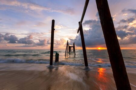 Long exposure image of Dramatic sky seascape with Old wooden pole in the sea sunset or sunrise scenery backgroundの写真素材