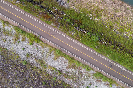 Aerial view top down photo from flying drone of asphalt road around the dam and people running...
