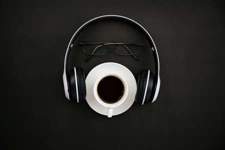 Top view of white coffee cup with headphone and teacher glasses on black paper backgroundの写真素材