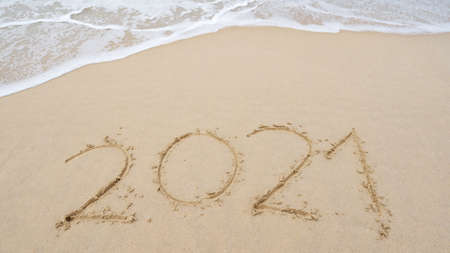 Happy New Year 2021 Text on the beach, 2021 year message hand written in sand on beautiful beach Waves crashing on sandy shore background. New Years concept.の写真素材
