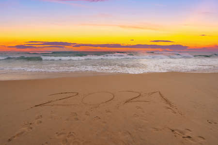 Text 2021 Lettering on the beach with waves and sunset sky Numbers 2021 year on the seashore, Message hand written in the golden sand on beautiful sunset or sunrise golden sky backgroundの写真素材