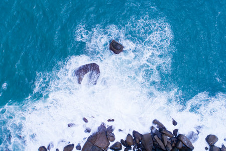 Aerial view Top down seashore big wave crashing on rock cliff Beautiful dark sea surface in sunny...