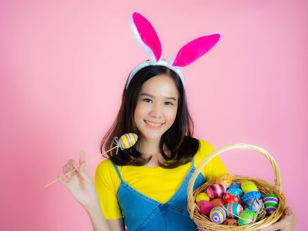 Portrait of a happy young woman wearing Easter bunny ears prepares to celebrate Easter on a pink background.の写真素材