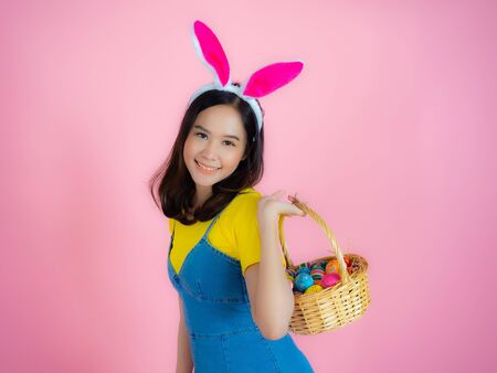 Portrait of a happy young woman wearing Easter bunny ears prepares to celebrate Easter on a pink background.の写真素材