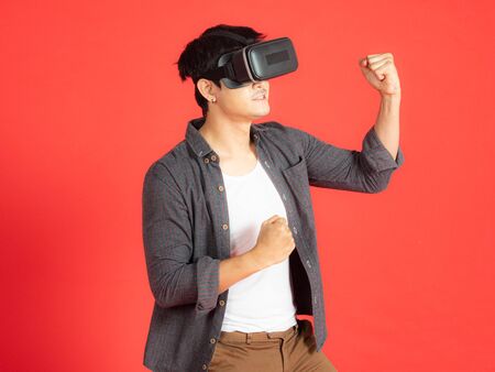 Young Man Wearing VR Headset and exploring another world isolated on red backgroundの写真素材
