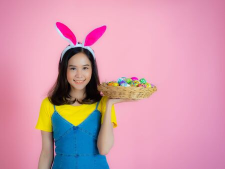 Portrait of a happy young woman wearing Easter bunny ears prepares to celebrate Easter on a pink background.の写真素材