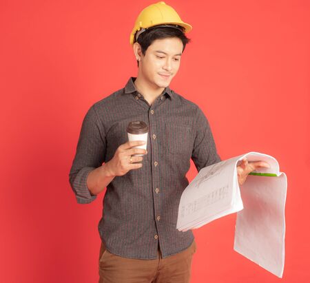 The young civil engineer is considering the construction plan while enjoying coffee. Portrait people concept on red backgroundの写真素材