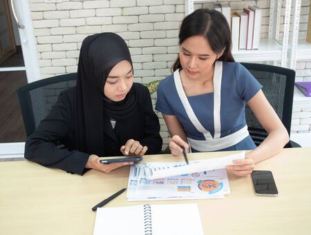 Two Asian businesswomen Sitting, discussing, and evaluating modern business operations at work. Muslim businesswomen work concept.の写真素材