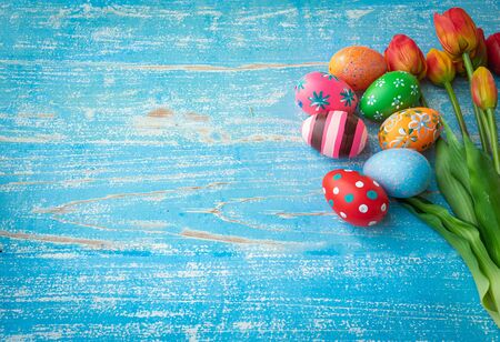 Beautifully colored eggs and patterns are arranged, along with yellowish-red tulips on old blue wooden boards, decorated for Easter.の写真素材