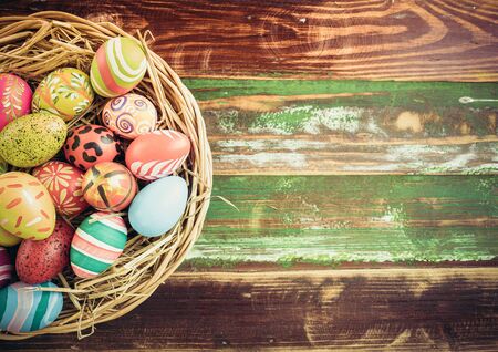 Easter eggs in various patterns and colors in a bird's nest placed on a wooden floor decorated in retro style.の写真素材