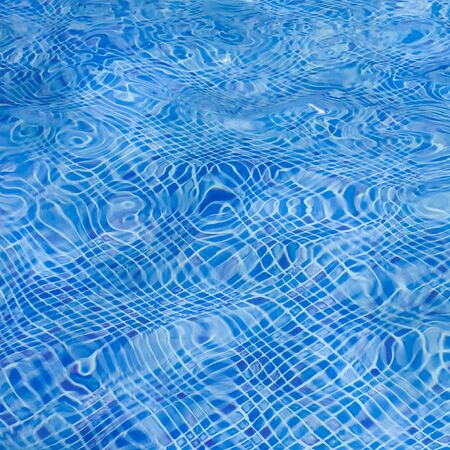 The light reflected on the top of the water surface of the pool lined with blue mosaic tiles below. Water ripples on blue-tiled swimming pool background.の写真素材