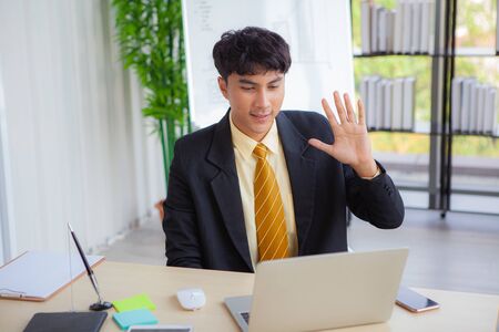 Young businessmen are greeting business partners on a computer screen via teleconferencing during the coronavirus (COVID-19) crisis.の写真素材